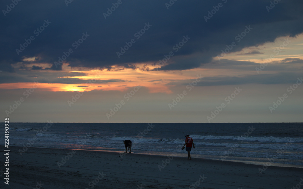 Friends walking down the beach looking for sea shells on a sun rise