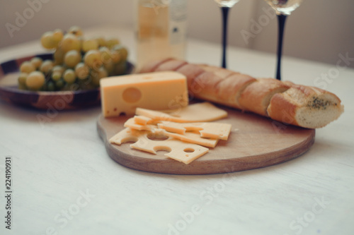 white wine,green gpapes in the plate,slaced cheese and baguette on the cutting board/ 