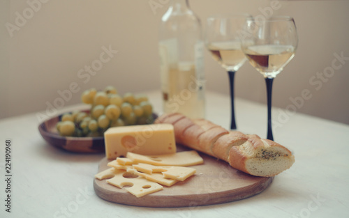 white wine,green gpapes in the plate,slaced cheese and baguette on the cutting board/  photo