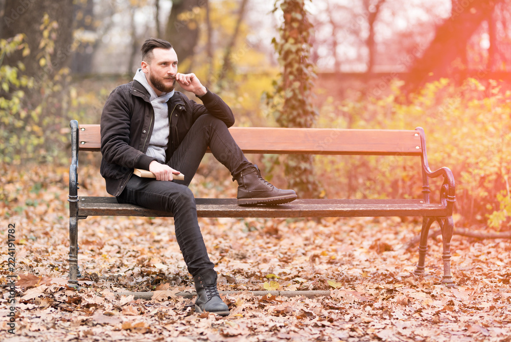 A handsome young hipster man sitting on a bench and adjusting his moustaches. A handsome young hipster man sitting on a bench and adjusting his moustaches.
