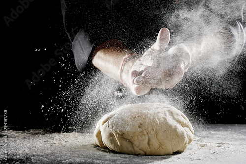 Man sprinkling white flour over blob of dough