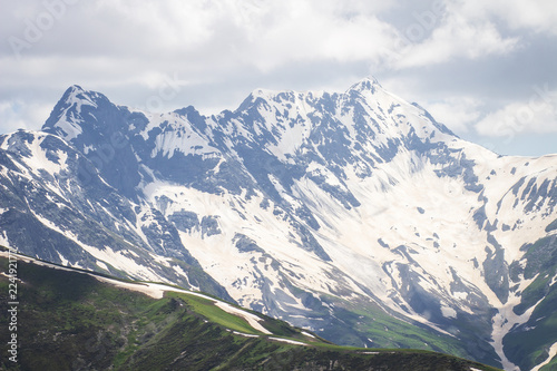 Snowy mountains range. Rocky mountain peaks in cloudy sky. View on Caucasus highlands.