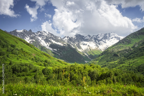 Mountains landscape. Rocky mountains with snowy peaks, green hills covered by grass in Alpine scene on bright sunny day with blue sky and clouds. Svaneti mountain landscape in Georgia. Amazing nature © dzmitrock87