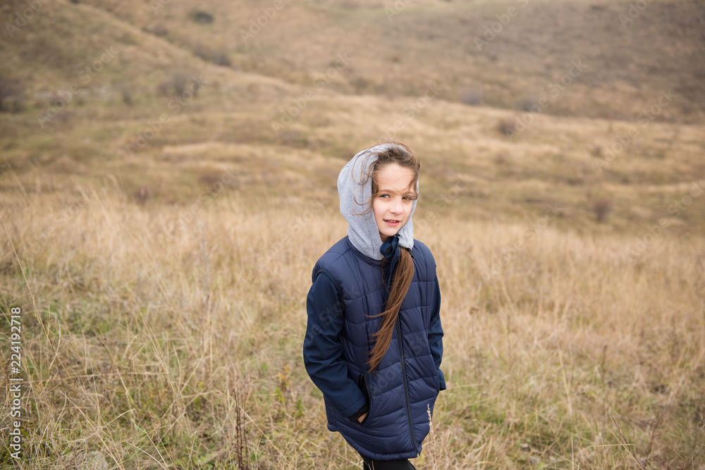 sport cute caucasian little girl in jacket with hood in windy mountains during hiking