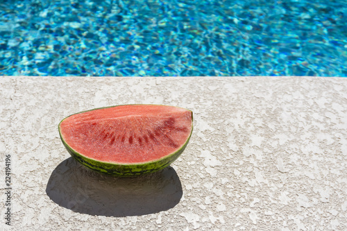 half watermelone on concrete patio against blurry water background photo