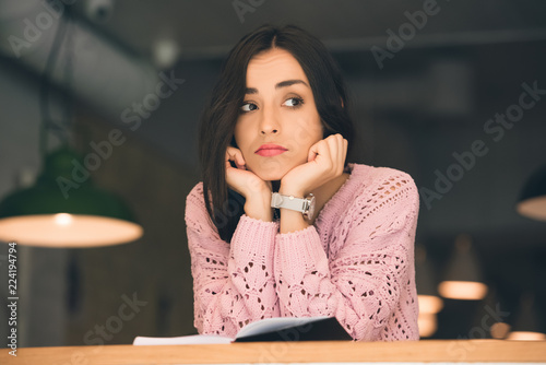 selective focus of upset young woman sitting with book at table in cafe