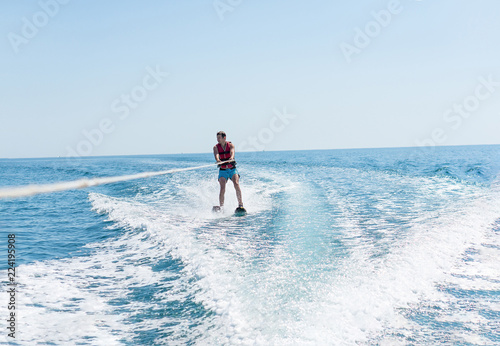 Young man glides on water skiing on the waves on the sea, ocean. Healthy lifestyle. Positive human emotions, feelings, joy.