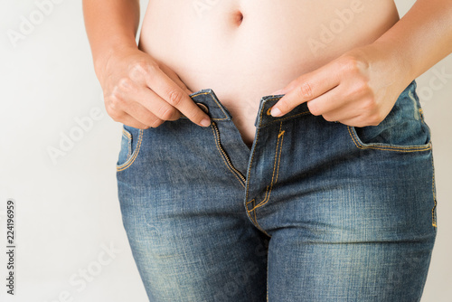 Overweight fat woman wearing jeans. Weight loss stomach closeup. Skinny jeans on a healthy slim fit body. Diet concept.