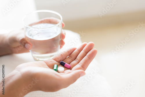 Closeup woman hand with pills medicine tablets and glass of water for headache treatment. Healthcare  medical supplements concept.