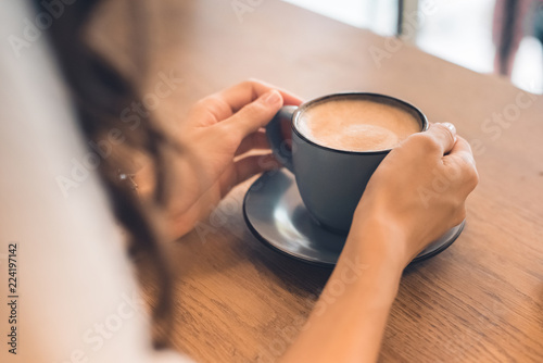 partial view of woman sitting with coffee cup at table in cafe