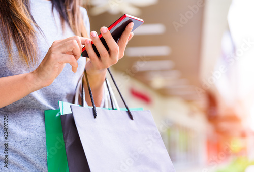 Woman holding shopping bags doing online shopping on her mobile phone in the supermarket. Black Friday sale concept.