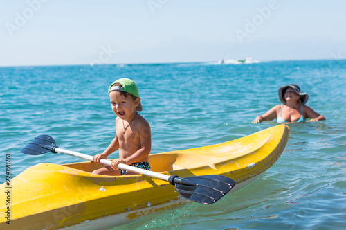 Grandmother and grandson smiling little baby boy in green baseball cap kayaking at tropical ocean sea in the day time. Positive human emotions, feelings, joy.