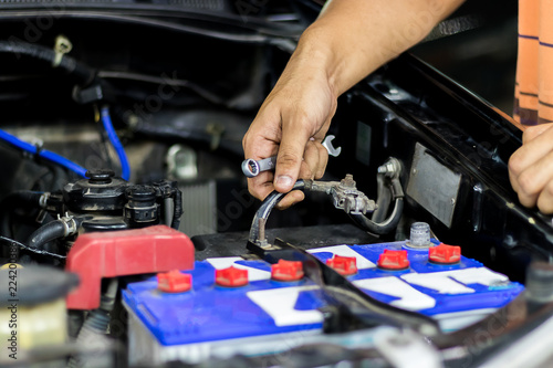 A man are removing the battery terminals from the car to work on the car electrical system using a wrench.
