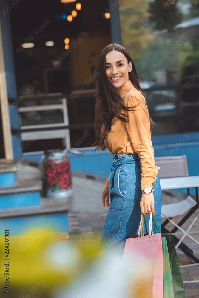 selective focus of stylish young woman walking with shopping bags at city street