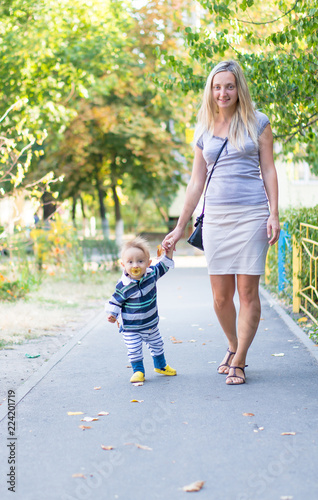 Happy mother and little baby boy playing with yellow leaves in the park. First steps son. Autumn. photo