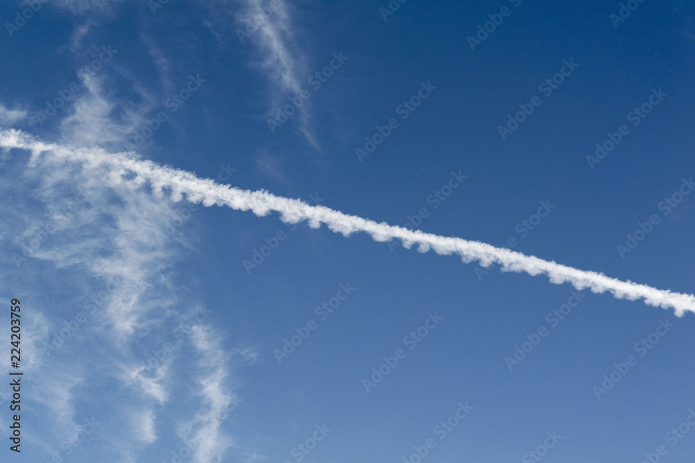 White trace of a flying plane in the blue sky White trace of a flying plane in the blue sky