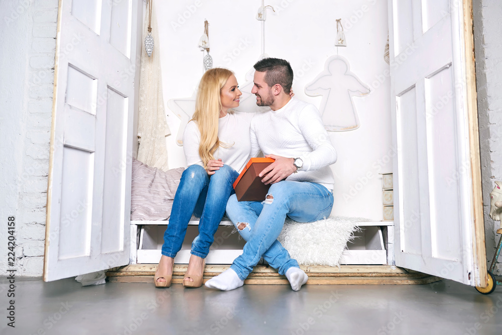 A beautiful happy young couple sitting in a wardrobe with christmas decorations and giving presents to each other. A beautiful happy young couple sitting in a wardrobe with christmas decorations and giving presents to each other.