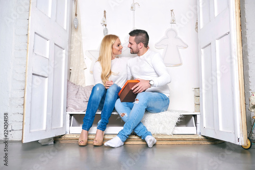 A beautiful happy young couple sitting in a wardrobe with christmas decorations and giving presents to each other.