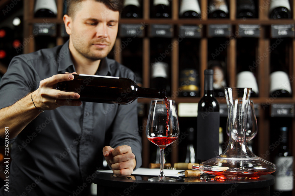 Sommelier pouring red wine from bottle in glass