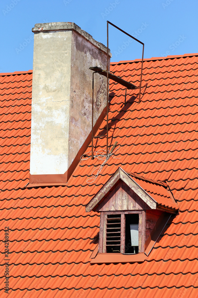Part of sunlit red tile roof with old chimney and vintage style window