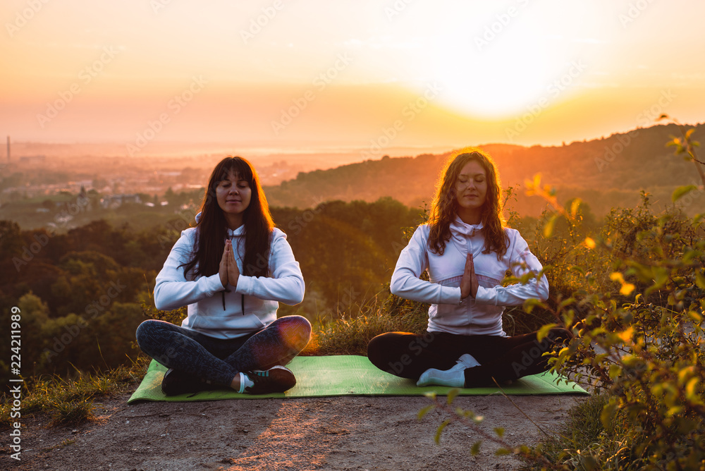 couple of women sitting at the edge of the hill. do yoga exercises on sunrise
