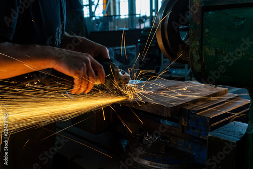 The worker polishes the metal with a grinding machine and sparks close-up.