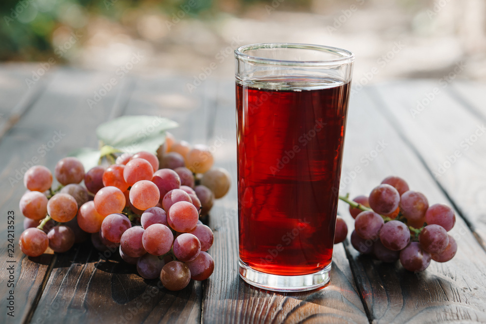 Fresh red grape juice and grapes on wooden garden table, refreshing organic beverage Fresh red grape juice and grapes on wooden garden table, refreshing organic beverage