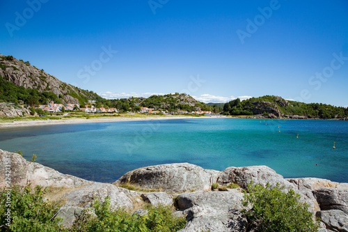 Serene scandinavian summer landscape of little village on south coast of Norway. Sunny sand and rocky beach with turquoise quiet water.