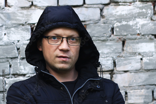 Portrait of the mature man in a hood against the background of an old brick wall.