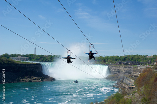 NIAGARA FALLS, ONTARIO, CANADA - MAY 21st 2018: Two people taking zipline ride at Niagara Falls in summer with Horseshoe Falls in background