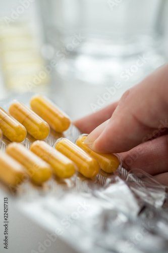 Frau nimmt gelbe Kapsel Tabletten aus Pillen Blister mit Wasser Glas