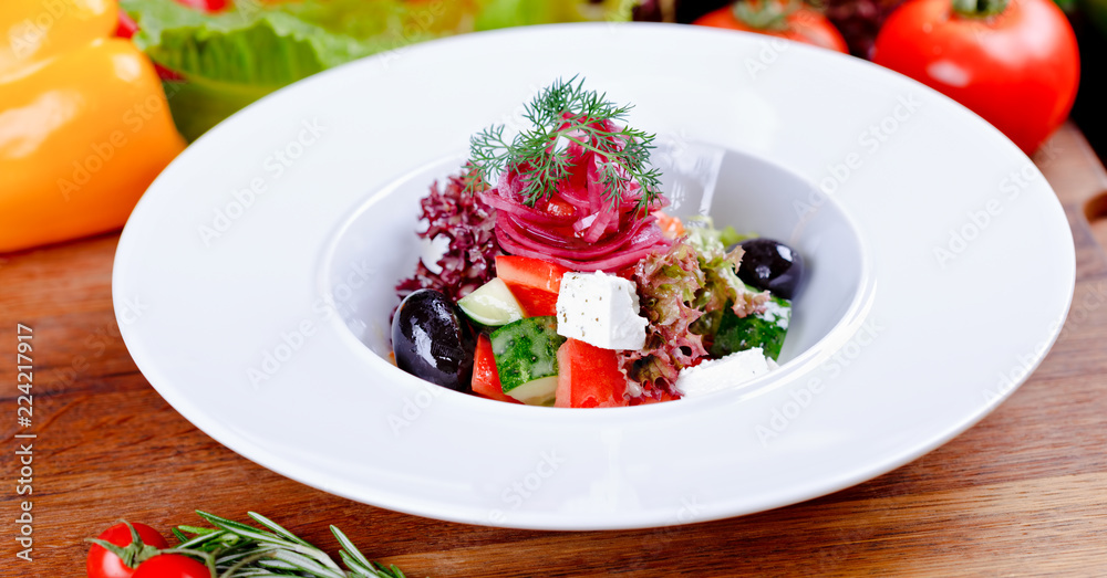 Greek salad with fresh vegetables, feta cheese and black olives on white plate. Close up. Greek salad with fresh vegetables, feta cheese and black olives on white plate. Close up.