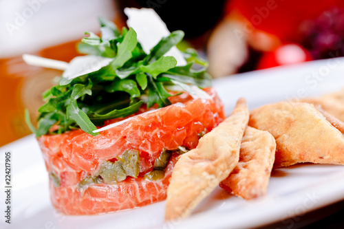 Salmon tartare with capers, arugula salad and parmesan cheese on white plate.