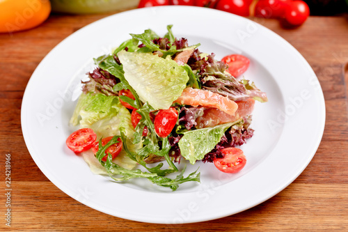 Salad with smoked salmon, cherry tomatoes, lettuce and arugula on white plate