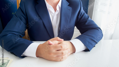 Closeup image of wealthy successful businessman in blue suit sitting with folded hands at modern office