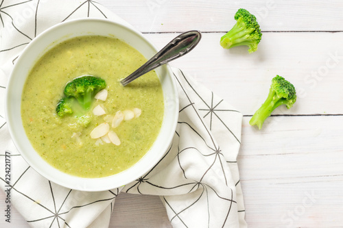 A bowl of soup with fresh broccoli on top, served on a white kitchen table, top view. photo