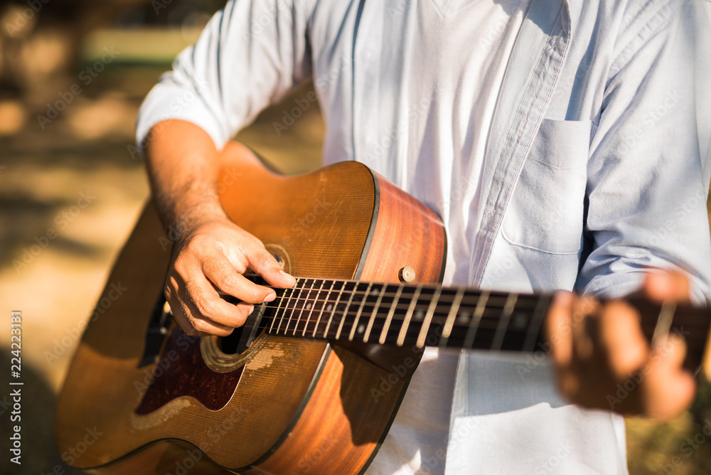 Young handsome asian man playing guitar in park. Outdoor lifestyle.