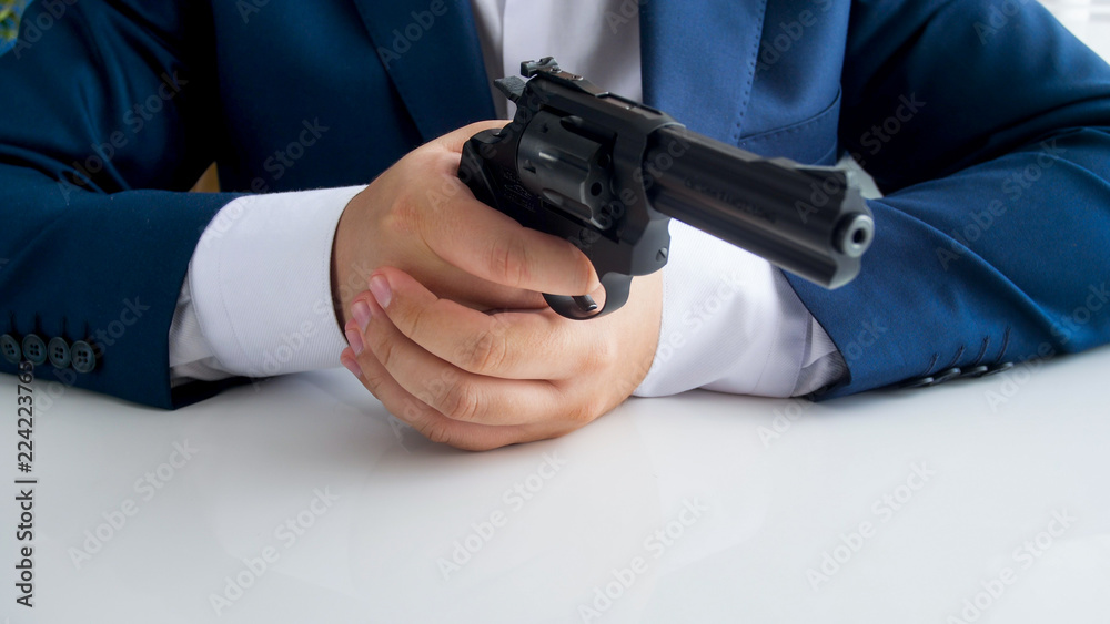Closeup image of man in suit sitting behind office desk and aiming with revolver Closeup image of man in suit sitting behind office desk and aiming with revolver