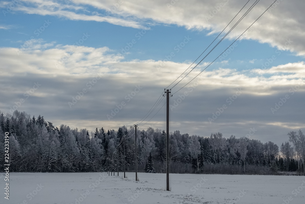 winter morning in the countryside, the sun illuminates the sky in different colors, all covered with snow, the field is visible electricity poles,but the back of the background can be seen the forest.