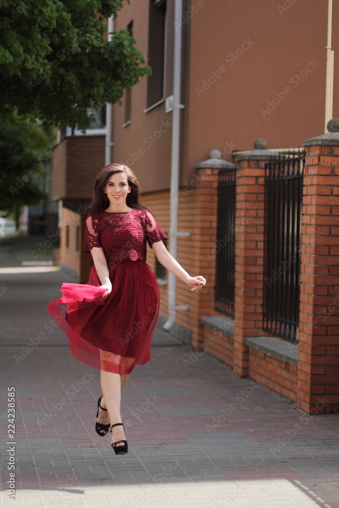 Happy beautiful woman in red summer dress walking and running joyful and cheerful smiling in the street 