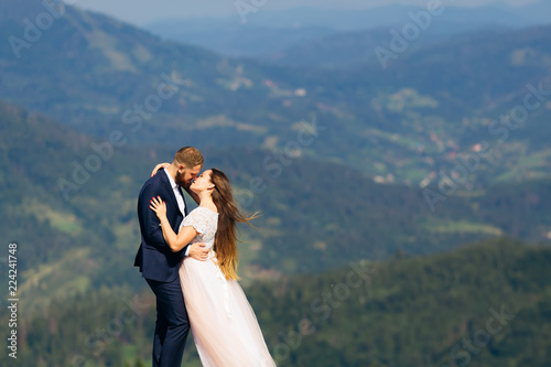 gentle kiss of newlyweds on top of the mountain and the wind blowing the hair of the bride