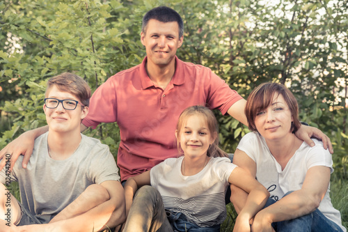 Happy European family embracing together outdoors portrait in summer park sitting on grass