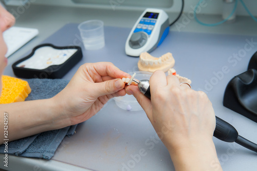 process of grinding the jaw during production. The dental technician processes artificial teeth with a micromotor. photo