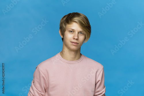 Close up portrait of smiling blonde teenager in pink blouse against blue background