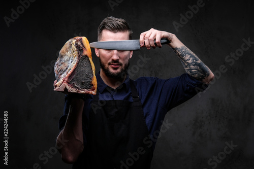 Chef cook holds the knife and large piece of exclusive cured meat on a dark background.