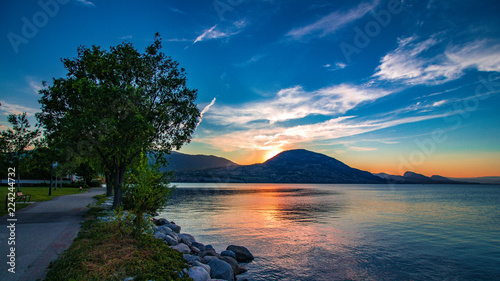 Photos watching from penticton park as the sun sets behind a mountain onto okanagan lak
