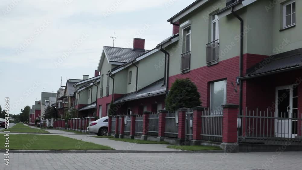 Camera showing of clapper board claps and in distance mature, dark haired man in white t-shirt and grey pants with tool box starts walking along porches of two-storey concrete houses in daylight