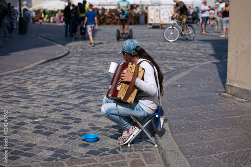 Sad girl street musician playing small accordion at the corner of the central sqaure