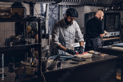 Two brutal cooks dressed in uniforms preparing sushi in a kitchen.