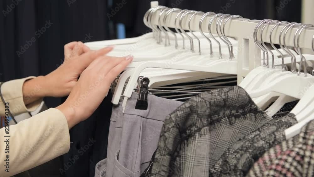 Close-up of female hands plucked a hanger with clothes. Woman's hands run across a rack of clothes. Slow motion shot from the side. Woman's hand smoothing clothes. Close-up of female hands plucked a hanger with clothes. Woman's hands run across a rack of clothes. Slow motion shot from the side. Woman's hand smoothing clothes.